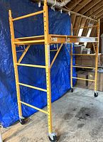 Front view of assembled yellow steel scaffolding with plywood deck and casters