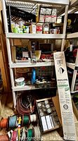 Overview of plastic shelving fully stocked with multiple electrical items including light bulbs, wire spools, electrical connectors, plugs, and tape