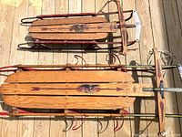 Two vintage Flexible Flyer sleds laying on wooden decking showing overall condition and size difference.