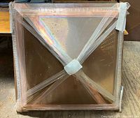 Copper cupola top viewed from above with wooden framing and cross brace visible, wrapped in protective plastic.