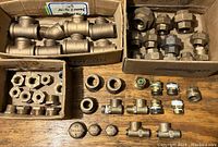 Top view showing various brass plumbing fittings including union fittings, caps, elbows, and small fittings arranged on a wooden surface with some boxes.