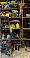 Full lot with ropes, straps, chains, pulleys, hooks, winches and bolt cutters on shelves and crates.