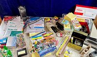 Overview of the home office supplies laid out on a table showcasing various packs of paper, staples, push pins, tape rollers, pencils, sticky notes, and hole punchers.