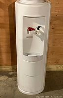 Full view of tall, white hot/cold water dispenser against wooden wall, showing front and general shape