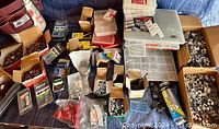 Wide overview of lot showing numerous boxes, plastic containers with fasteners, screws, hex nuts, and related hardware items arranged on a surface.