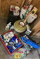 Porcelain toilet with tank, seat, multiple bottles of septic treatment in various sizes and brands, and assorted plumbing parts and accessories arranged on the basement floor near a wooden wall.