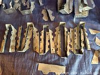 Wide view of several rows of U-shaped galvanized metal post caps and L brackets spread out on a surface, showing multiple pre-drilled holes for fasteners.