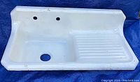 Front view of vintage white enameled cast iron sink with drainboard showing surface dirt and minor discoloration spots.