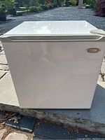 Closed front view of white Frigidaire compact bar fridge on outdoor surface.