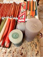View showing assortment of twisted taper candles in red, green, orange, and white along with smooth pillar and textured round ball candles on countertop.
