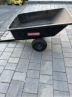 Front side view showing black polypropylene utility bed and one rubber wheel with Craftsman logo on side.