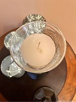 Close-up top view of a used white pillar candle with a burnt wick inside a glass candle holder with silver crackle finish.