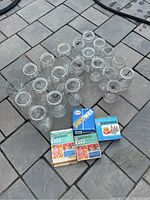 Top view of about 21 clear glass Mason jars arranged on a stone patio surface with three boxes of Esso Parowax wax positioned at the bottom.