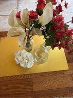 Top view of the artificial flower arrangements including white calla lilies, red flowers, white roses and empty clear glass vase on a yellow surface.