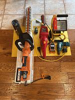 Wide view of lot showing WORX and Homelite hedge trimmers, work light, drill, and air cord on floor