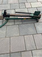 Side view of the Yardworks manual log splitter, showing the green metal frame, foot pedal and splitter head.