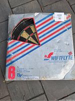 Original packaging of the Swiftflyte dart board showing branding, product information, and 6 brass darts included.