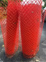 Two rolled-up orange plastic mesh safety fences standing upright on asphalt surface.