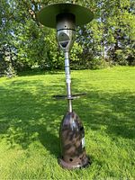Full view of standing outdoor propane patio heater with built-in round shelf and olive green top reflector, placed on grass.