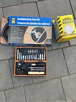 Powerfist Sandblasting Gun Kit box with hose, gun and accessories laid out, box of disposable dust masks next to it.