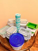 Various stacked plastic food containers with snap-lock lids, a roll of reusable plastic storage bags, and a large round container with blue lid printed with Olaf from Frozen character.