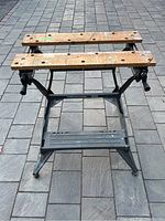 Front view of used Black and Decker Workmate 300 workbench on stone surface, showing wooden top boards and metal frame.