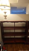 Full view of the wood bookshelf showing its height and shelves, with a lamp placed on top for scale.