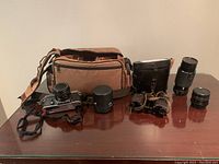Full set showing camera, binoculars, lenses, case and carry bag displayed on a wooden table
