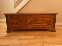 Front view of the wooden cedar chest showing metal corner accents and wood grain on the front panel.