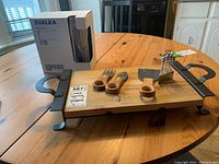 Cheese serving tray on wooden table with cheese knives, metal picks, and boxed wine glasses.