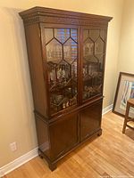 Full view of wooden china cabinet showing glass upper cabinet with geometric patterned panes and wooden lower cupboard doors.
