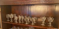 Shelf display of multiple crystal stemware glasses arranged in rows, with different bowl shapes and etched designs visible.