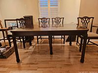 View of vintage dining table with four matching chairs around it, wood finish and ornate legs visible.
