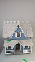 Front view of handmade wooden dollhouse showing blue facade, white roof shingles, and porch detail with railings