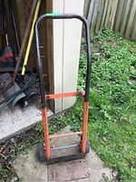 Full dolly hand truck outside a shed, showing the coated metal frame and curved handle bar.