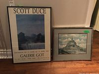 Two framed prints side by side, one Scott Duce gallery print with metal frame and a framed print of Mont Saint-Michel with wood frame.