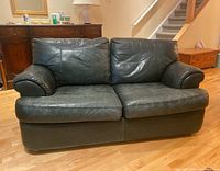 Front angle of black leather two-seat sofa showing seat cushions and armrests with normal wear.