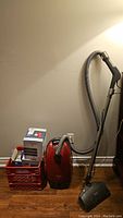 Red canister vacuum, milk crate with filter boxes, hose, telescopic wand, floor nozzle