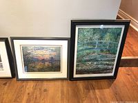 Two framed Monet prints side by side leaning against a wall on wood floor, showing the artwork and frame details.