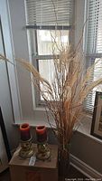 Photo of tall clear glass vase filled with tall dried sticks placed by a window, with the candle holders visible nearby.