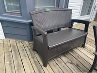 Full front view of resin dark brown outdoor bench showing the wicker pattern design, curved backrest, and armrests.