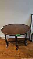 Full view of round wooden pie crust table with four legs and brass capped feet on hardwood floor against white wall.