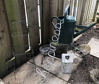 Photo showing all five items together outdoors: metal plant stand, watering can, ceramic candle holder, aluminum 'happiness' sign, and wire tomato cage.