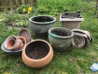Wide view of all assorted planters and dishes arranged on grass showing terra cotta, plastic, ceramic, and Pyrex items