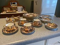 Overview of all pieces: stacked dinner plates, side plates, teacups on saucers, cream pitcher, sugar bowl, bowls on countertop