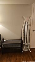 Shoe rack next to foldable ironing board in white metal frame