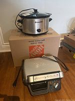 Bravetti slow cooker atop a cardboard box with power cord wrapped around it, showing the brand logo and control knob.
