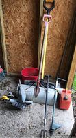 Photo showing the assortment of yard tools including Jerry can, shovels, bucket, watering can, and hand tools against wooden wall