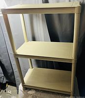 Photo showing a beige plastic three-tier utility shelf with vertical cylindrical legs and flat rectangular shelves.