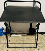 Front view of the black folding TV tray with metal frame and rectangular surface.